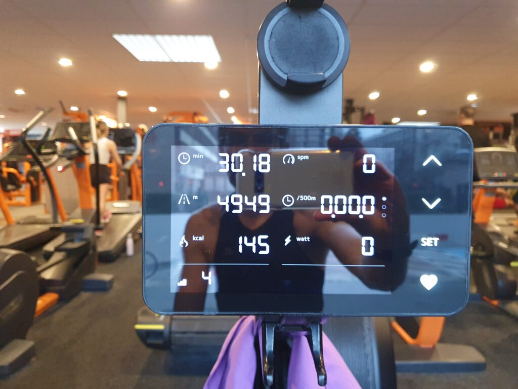 picture of an indoor rower control screen, showing a session of 30min, 4949m. i can been seen reflecting on the screen