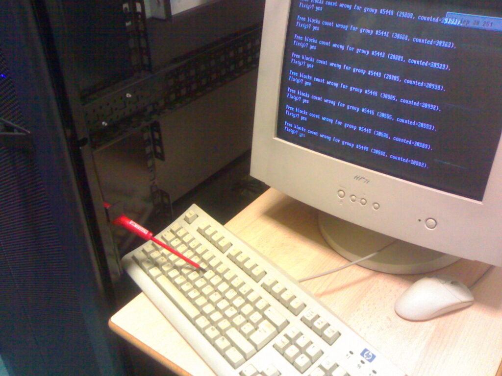 a crt monitor on a ttable, showing a bunch of fsck related messages. beneath a keyboard. a read screwdriver is holding the Y key down.