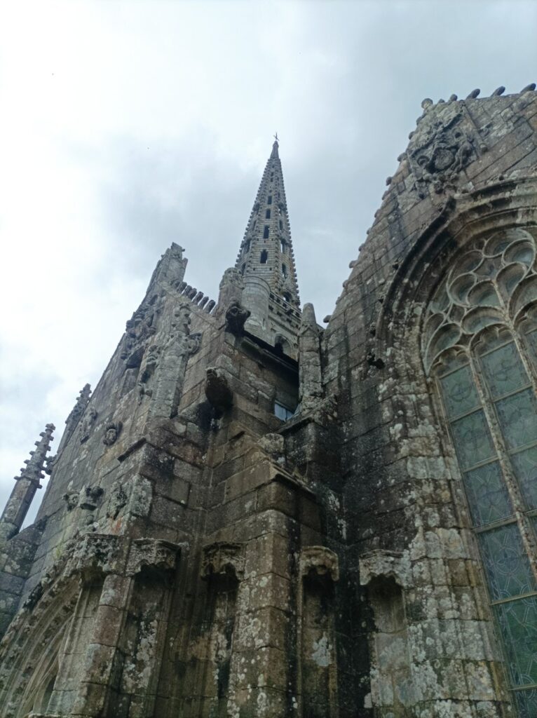 Granite stone church, breton gothic style, taken from below, at close range. So it lokks wuite massive and old, with a pointy stone belltower above